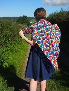 a woman is walking down a path with a crocheted shawl