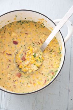 a pot filled with corn and potatoes on top of a table next to a spoon