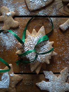 some cookies are on a wooden table with green ribbon and snowflakes around them