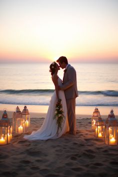 a bride and groom kissing on the beach with candles lit up in front of them