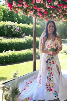 a woman in a wedding dress standing under a flower covered structure