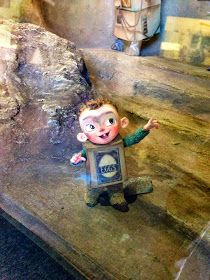 a small statue of a boy standing on top of a wooden table next to a rock