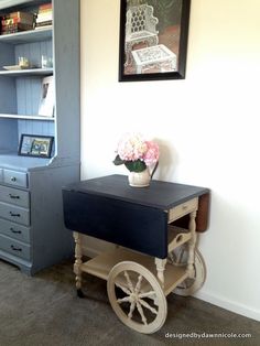 a small table with flowers on it in front of a bookshelf and bookcase