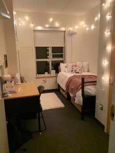 a small bedroom with lights strung above the bed and desk in front of the window