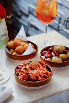 three bowls of food on a table next to a glass of wine and a drink