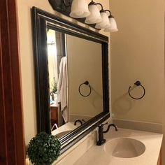 a bathroom sink under a large mirror next to a light fixture and towel dispenser