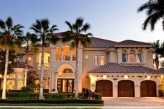 a large house with palm trees in the front yard and driveway at dusk, surrounded by lush greenery