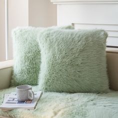 two green pillows and a book on a bed with a window in the back ground