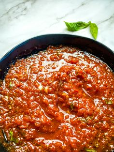 a skillet filled with sauce on top of a white marble counter next to a green leafy plant