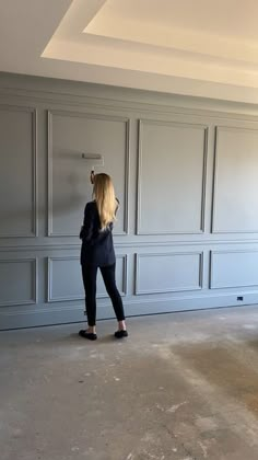 a woman is standing in an empty room and pointing at the wall with her finger