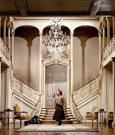 a man is walking up the stairs in a large room with chandelier and chairs