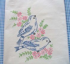 two birds sitting on top of a blue and white checkered tablecloth with pink flowers