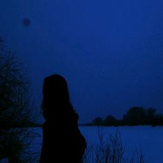 a woman standing in the snow at night with her back turned to the camera and looking out