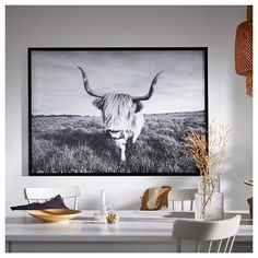 a black and white photo of a long horn cow in a field is hanging above a dining room table