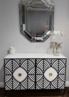 a white and black cabinet with a mirror above it on the wall next to a vase