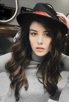 a woman with long brown hair wearing a black hat and grey turtle - neck sweater