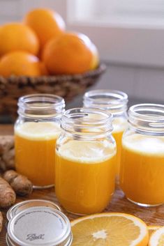 several jars filled with orange juice sitting on top of a wooden table next to nuts