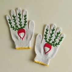 two white gloves with red and green designs on them, one has a radish in the middle