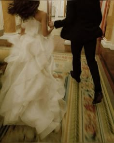 a bride and groom are walking down the hall together in their wedding gowns, carrying an umbrella