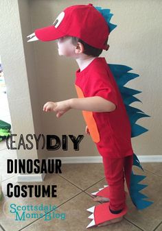 a young boy in a red dinosaur costume standing on the floor with his arms out