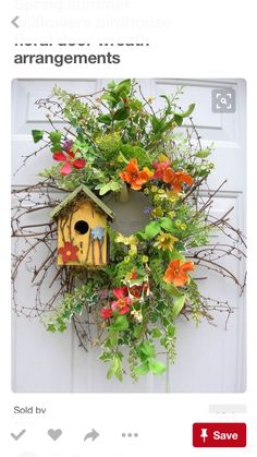 a birdhouse is hanging on the front door with flowers and greenery around it