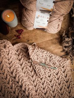 yarn and scissors on a wooden table next to a candle, tea pot and knitting needles