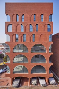 an unusual brick building with arched windows and cars parked in the parking lot below it