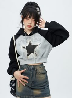 a young woman with black hair wearing a grey and black hoodie is standing in front of a white background