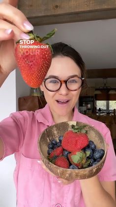 a woman holding a bowl full of berries and strawberries