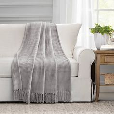 a white couch with a blanket on top of it next to a table and potted plant