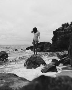 a woman standing on top of rocks near the ocean