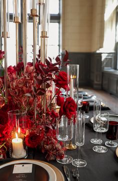 the table is set with red flowers and candles