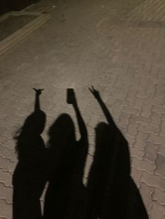 the shadow of two people holding their hands up in the air on a brick road