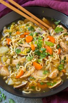 chicken noodle soup in a black bowl with chopsticks on the side and purple cloth