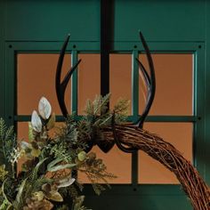 a wreath with antlers and greenery hanging from the front door to make it look like an antler's head