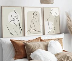 three framed nude female art prints on a wall above a bed with pillows and blankets