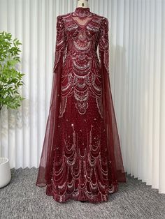 Elevate your evening with this stunning burgundy beaded gown, a masterpiece of intricate design and luxurious craftsmanship. The dress boasts an elegant high neckline and long, flowing sleeves that add a touch of regal sophistication. The sheer overlay is meticulously adorned with cascading beadwork, creating a mesmerizing pattern that sparkles with every movement, ensuring all eyes will be on you.Designed for the discerning fashionista, this gown offers a perfect balance of classic charm and contemporary flair. The semi-sheer bodice brings a subtle hint of allure, while the fully lined skirt provides comfort and modesty. The beaded artwork is a testament to exquisite attention to detail, making this dress a unique piece for special occasions, from glamorous galas to exclusive soirées.Pair Beaded Artwork, Dinner Gown, Flowing Sleeves, Luxury Dresses, Patterned Tights, Solid Leggings, Sheer Overlay, Beaded Gown, Lined Skirt