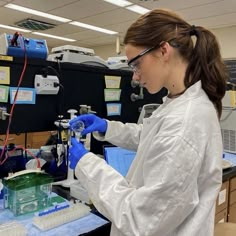 a woman in white lab coat and goggles working on a pipe with blue liquid