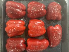 six red peppers in a baking pan with seasoning on the top and bottom half