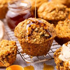 some muffins are sitting on a cooling rack with honey and jam in the background