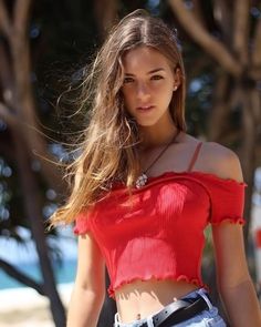 a beautiful young woman in a red top posing for the camera with her hair blowing in the wind