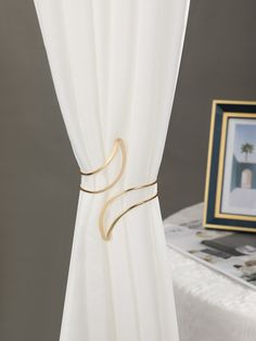 a white curtain with gold metal hardware on it and a framed photo in the background