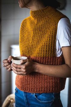 a woman wearing an orange and yellow knitted sweater holding a cup in her hands