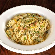 a white bowl filled with pasta and vegetables on top of a wooden table next to a fork