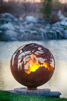 a fire pit sitting on top of a lush green field next to a lake and forest