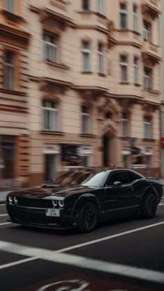 a black sports car driving down the road in front of a building with many windows