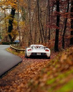 a white sports car parked on the side of a road in front of some trees