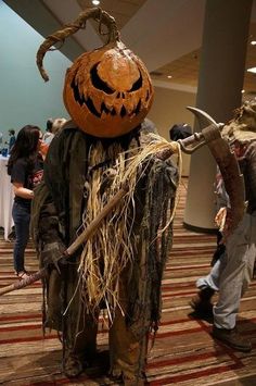 two people dressed up as scarecrows and one is holding a large pumpkin on his head