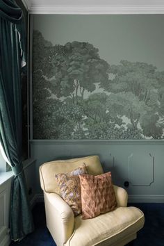 a chair with two pillows on it in front of a wallpapered tree pattern