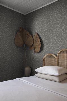 a bed with white sheets and pillows next to a wallpapered headboard in a bedroom